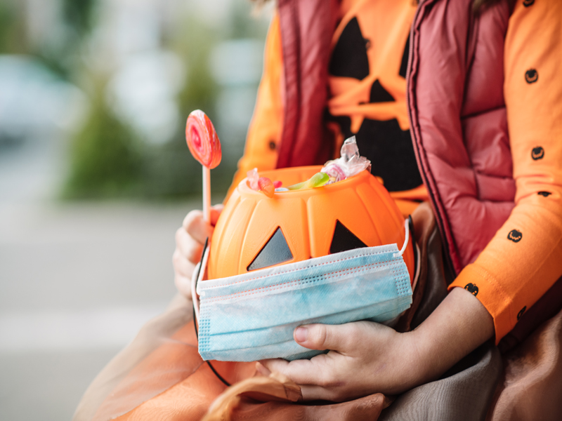 Woman sitting with a halloween bucket, a lolipop and a mask in her hand.